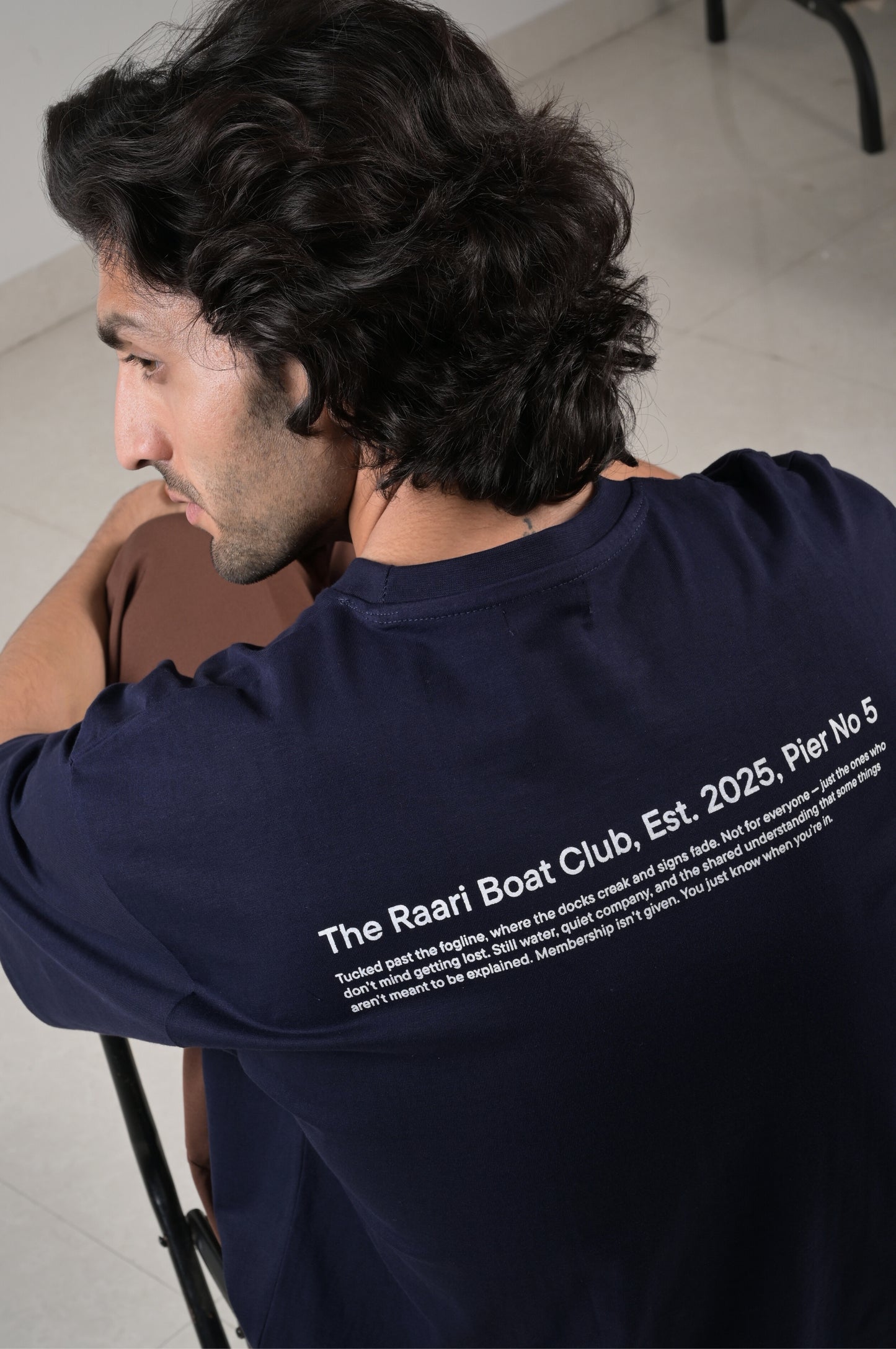 Man wearing a navy blue t-shirt with text on the back, sitting indoors.