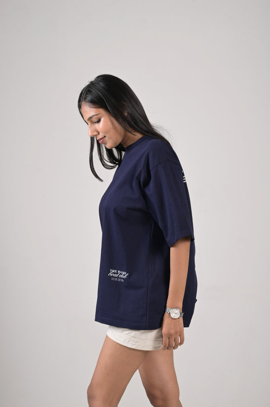 Woman wearing a navy blue t-shirt with a boat club print in the left hand bottom corner on a plain background